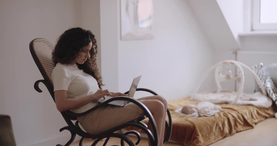 A woman works on her laptop as her baby sleeps nearby