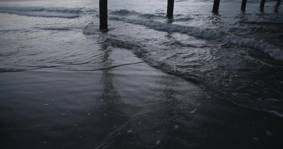 Small waves washing over the sand on a beach under a pier at evening