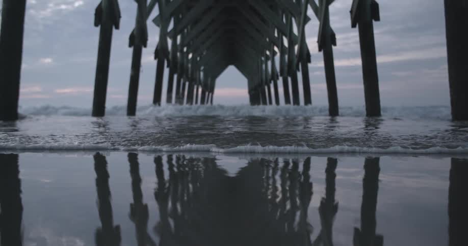 Ocean waves washing ashore a sandy beach beneath a pier