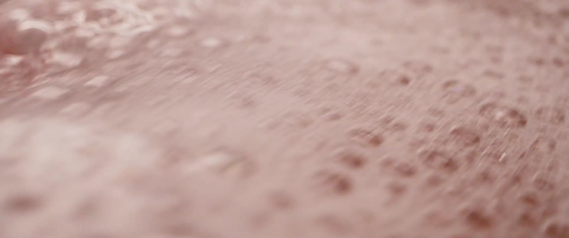 Close up of a layer of foam floating on the surface of water moving on a copper bowl