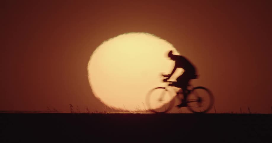 A person biking in front of a setting sun