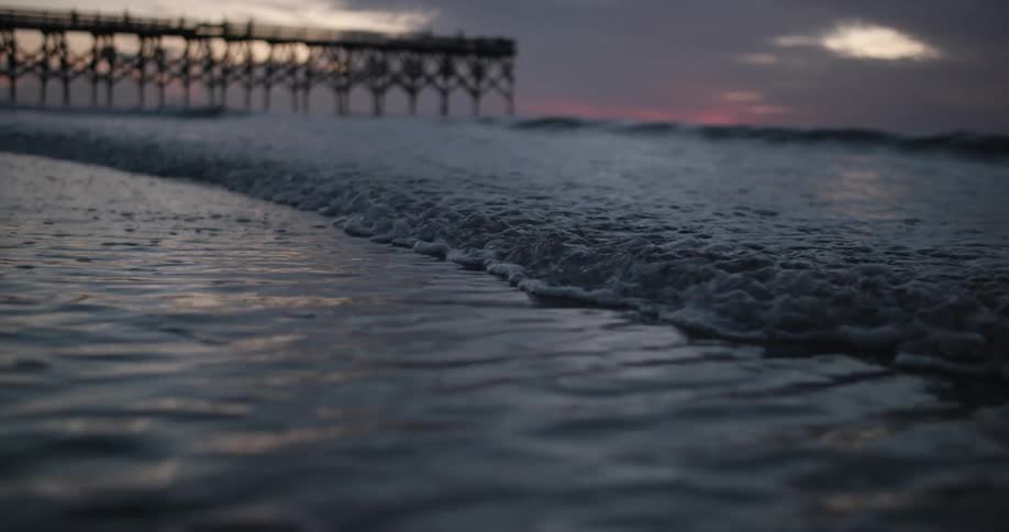 Small waves washing over the sand on a beach close to a pier at evening