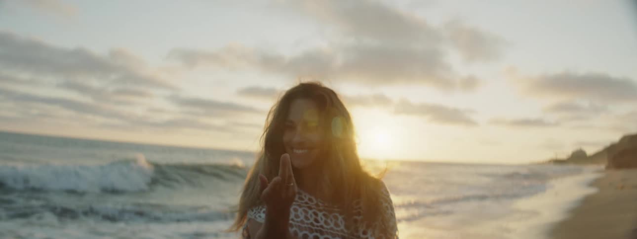 A woman spins and dances on the beach as sea waves crash behind her