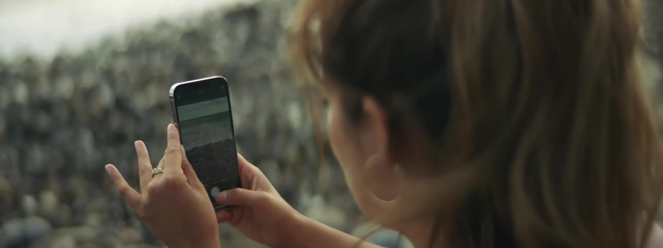 A woman taking a photo of a beach with her smartphone