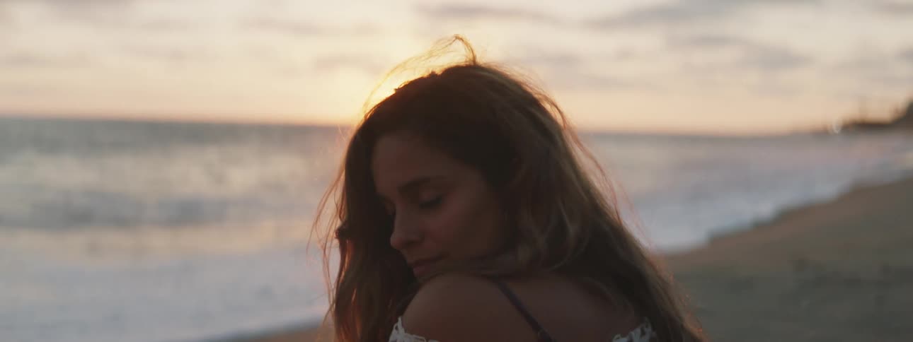 A woman sitting on the beach smiles and flips her hair around