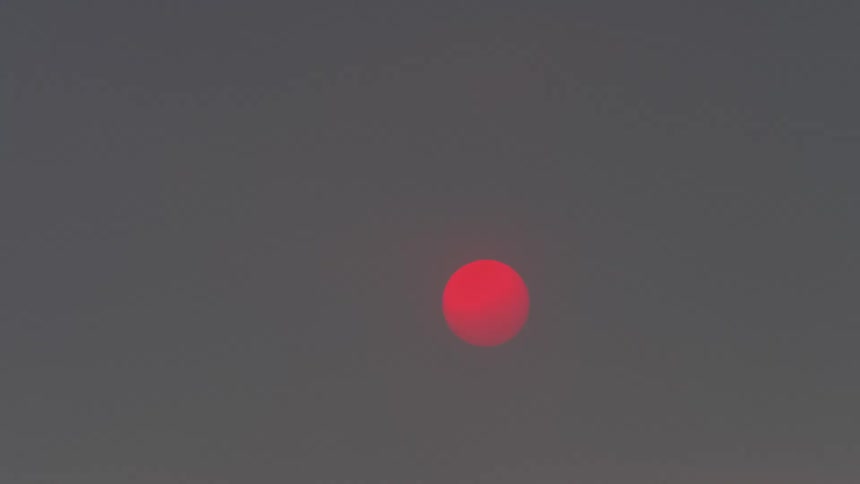 Bright red sun setting on a gray sky behind a thin layer of clouds