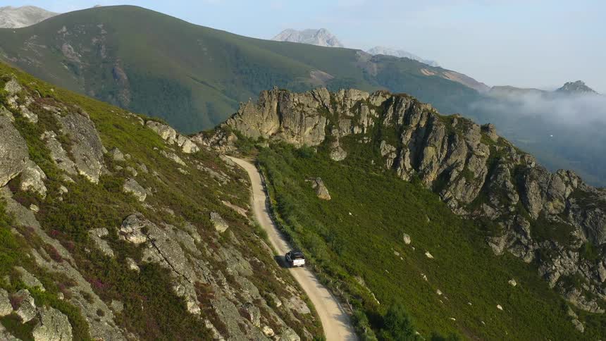A vehicle travels along a narrow road through the mountains during the day