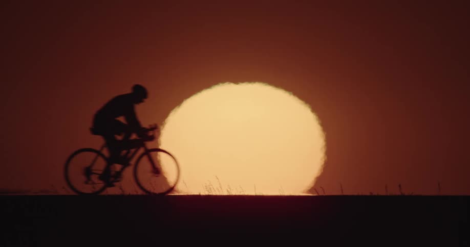A large glowing sun in a red sky creates a backdrop for the silhouette of a person riding by on a bike