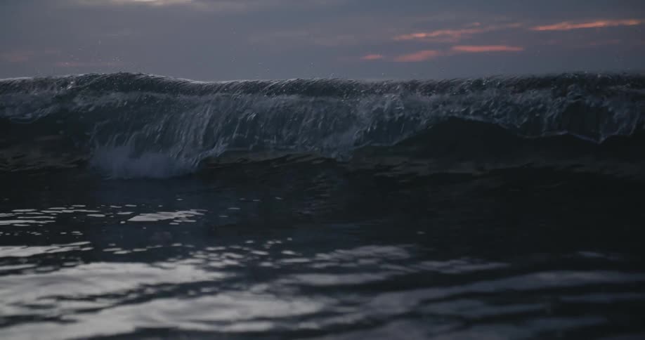 An ocean wave crashing in the sea at sunset