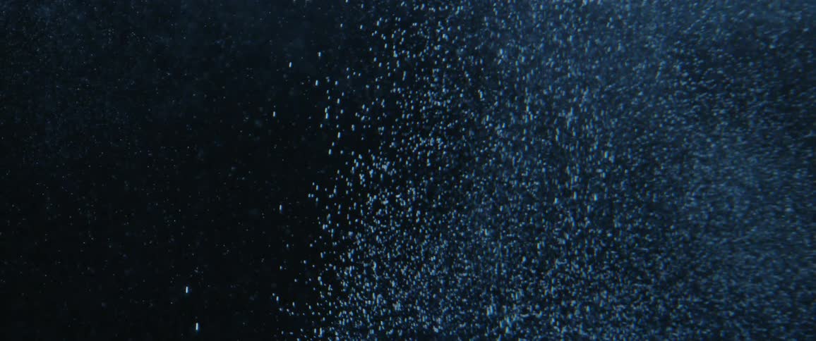Blue water is shown with a multitude of tiny bubbles creating a large cloud and floating to the surface