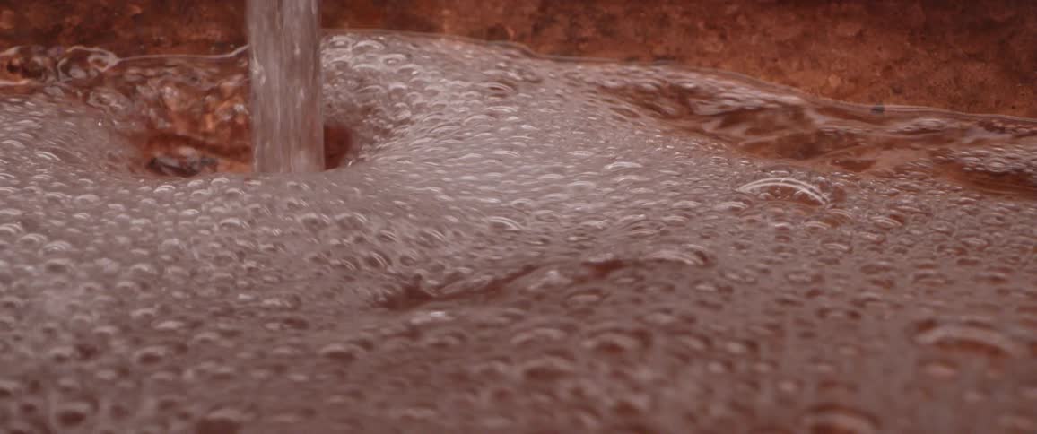 Stream of clear bubbling water filling up a copper bowl