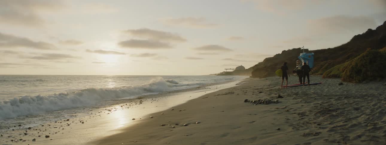 Three surfers gather their surfboards on the sand near the coast at morning
