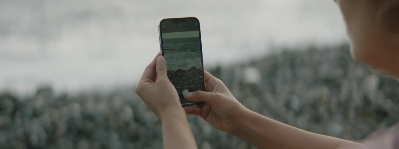 A woman taking a photo of ocean waves on a beach with her smartphone