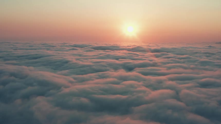 The sun shines brightly in a hazy sky above the clouds reflecting the colors of the sun rays
