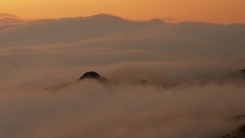 White thick clouds rolling over the peaks of a mountain range at golden hour