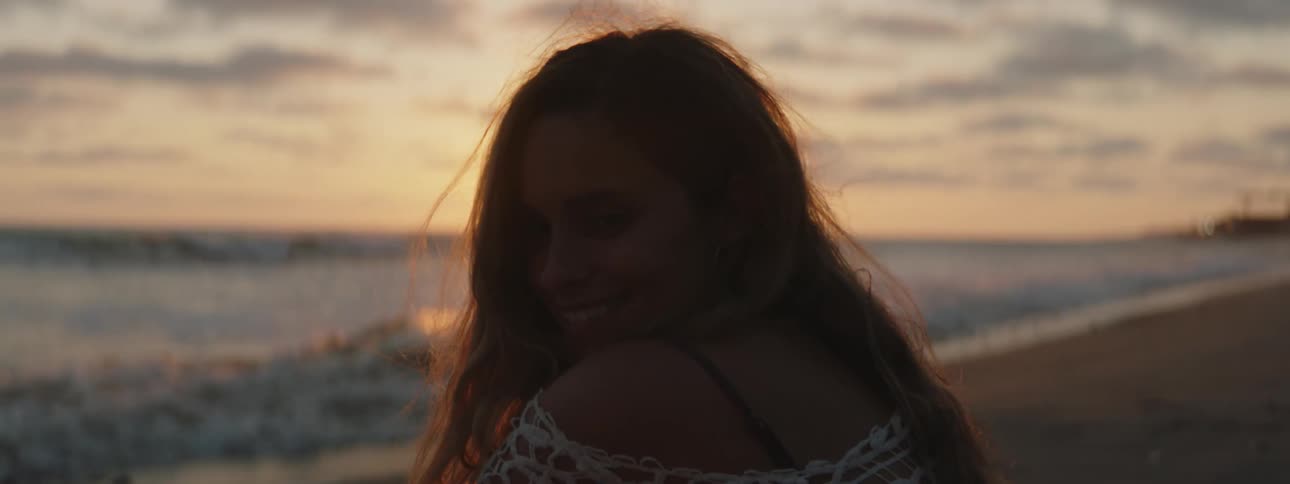 Woman sits on the beach partly silhouetted by the setting sun as the surf rolls onto the beach
