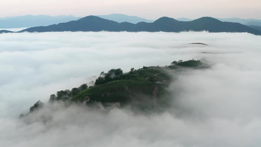 Green highland peaks through low lying clouds and taller mountains sit under red tinted sky on the horizon in Northern Spain