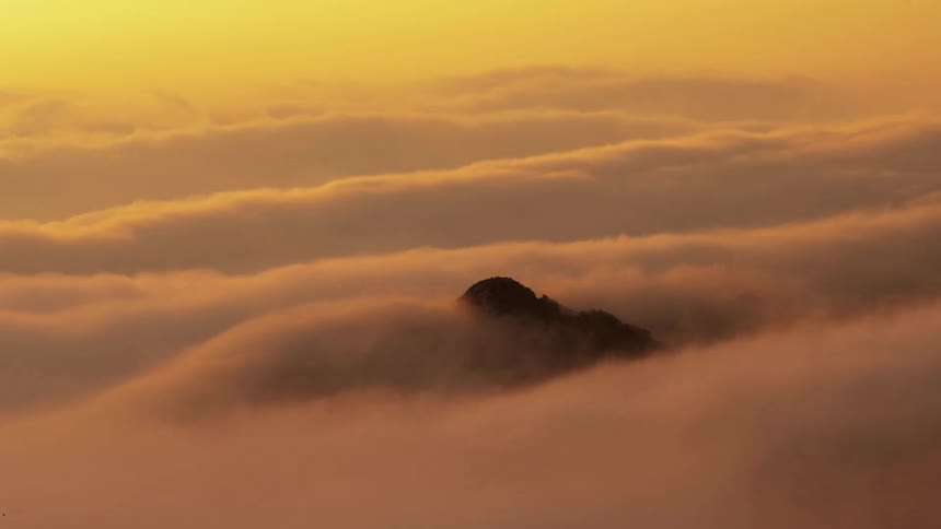 Time lapse of clouds washing over like ocean waves over the mountains at evening
