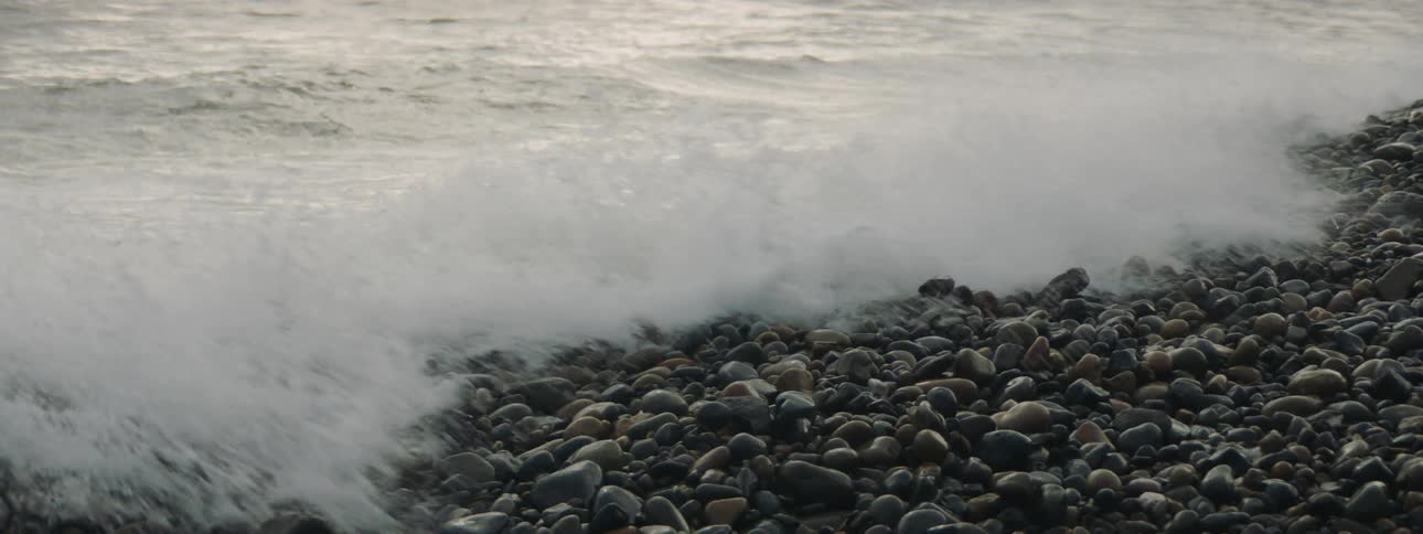 An ocean wave crashing into a pebbly beach