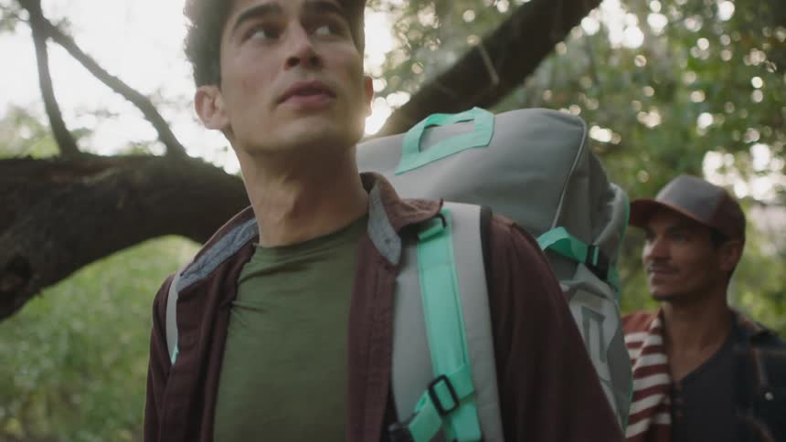 Men wearing crimson shirt gray backpack and cap hike in the green forest