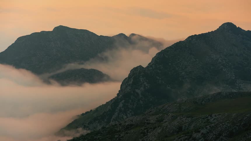 Clouds ebb and flow around the rocky peaks of a mountain ridge in the evening
