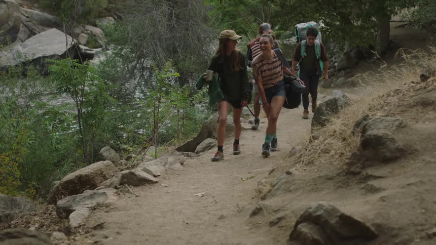 A small group of people are hiking on a trail on a hillside in the woods with a flowing river below