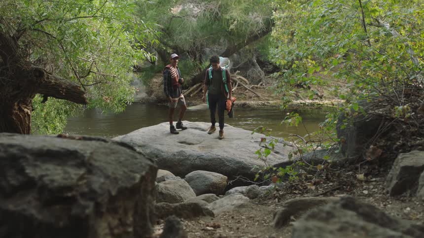 Teenage friends hiking near a river stand on a big rock waiting for the rest of the group