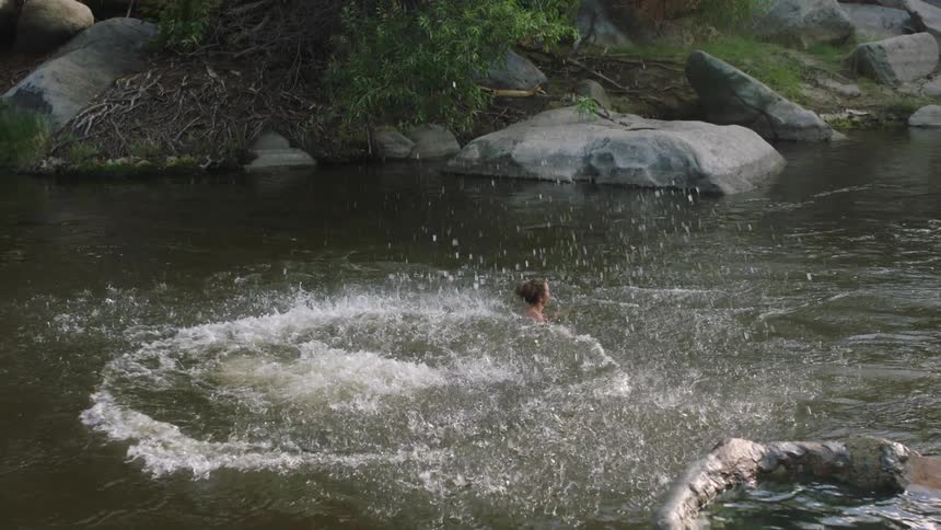 Two women in a lake watch as a man cannon balls in
