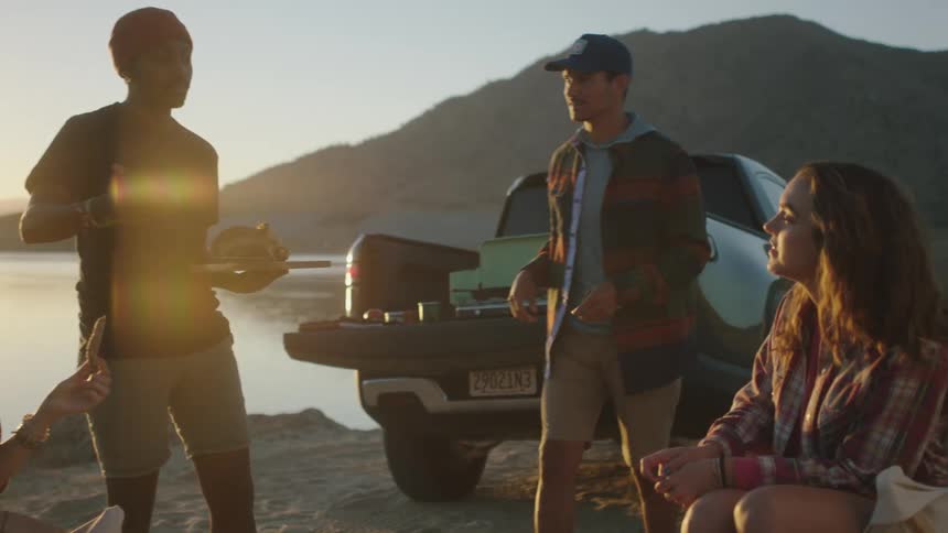 A group of friends chatting and eating while hanging out next to a lake