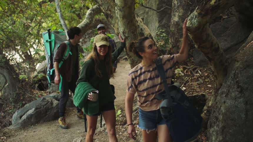 A group of four people are hiking through the woods and touching the trees and rocks as they walk