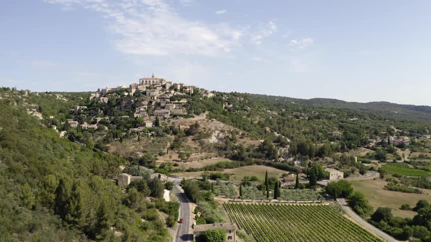 Automobiles travel on roads near the medieval buildings of the village of gordes built on a mountain