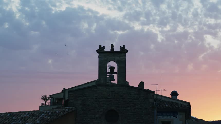 Birds fly around the bell on the top of a church