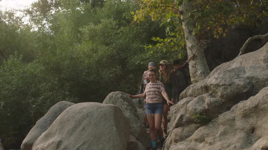 A small group of people are walking down a path through rocks and boulders out of the woods