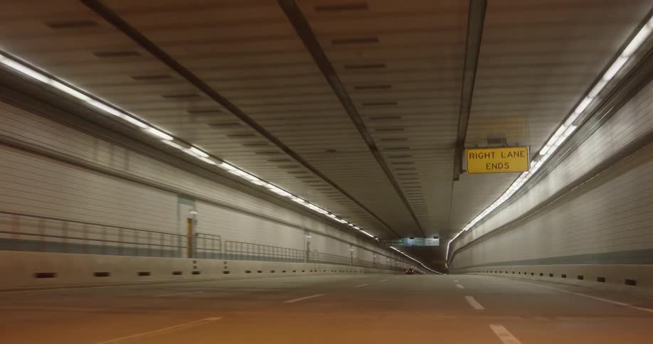 Overhead lights guide the way through a curvy tunnel in a city