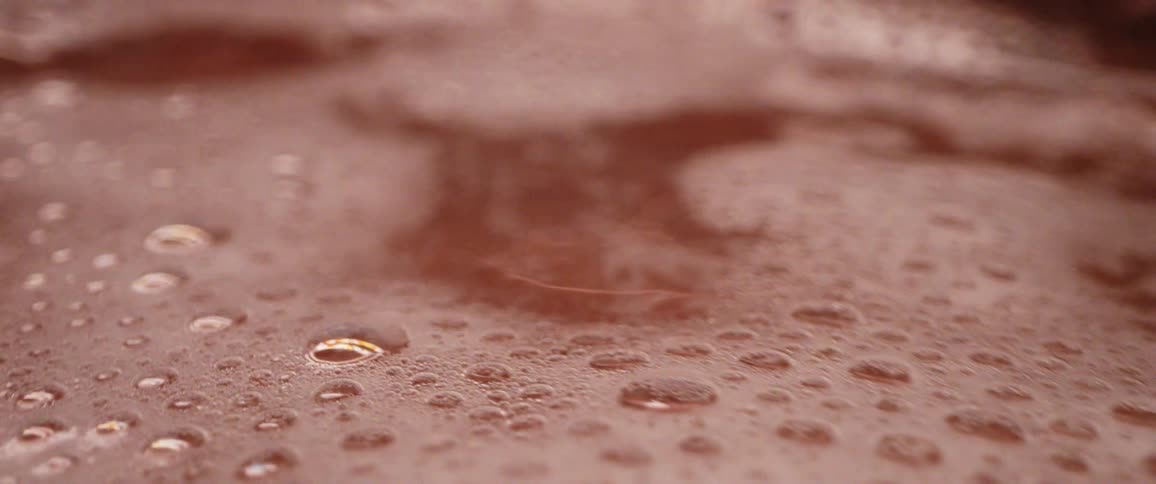 Close up of a layer of foam floating on the surface of water moving on a copper bowl