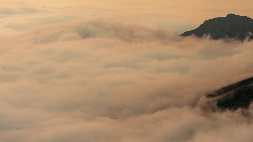 Time lapse of clouds rolling clouds washing over like ocean waves over the mountains at evening