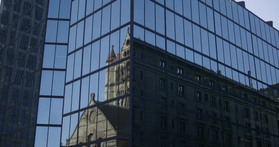 A stone building reflected in a glass skyscraper in a city