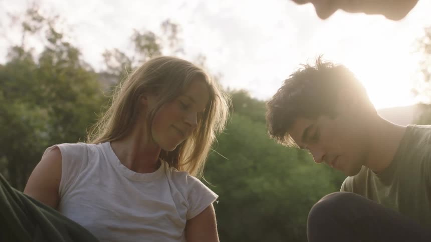 A woman takes her sweatshirt off in front of a river as she stands with a man and another woman
