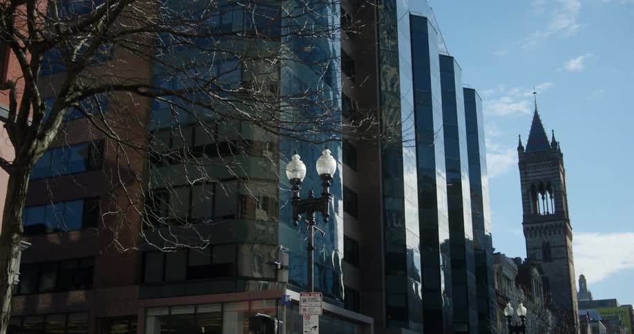 Automobiles travel on a road lined with buildings and a bell tower as they move into downtown