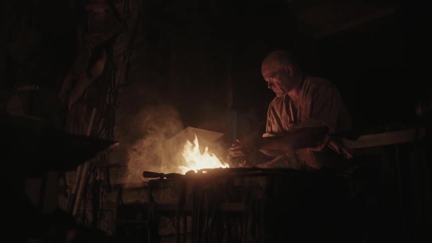 A blacksmith is arranging his tools and tending to his fire