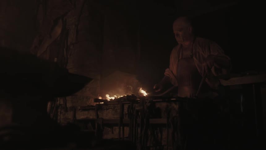 A blacksmith is arranging his tools and tending to his fire