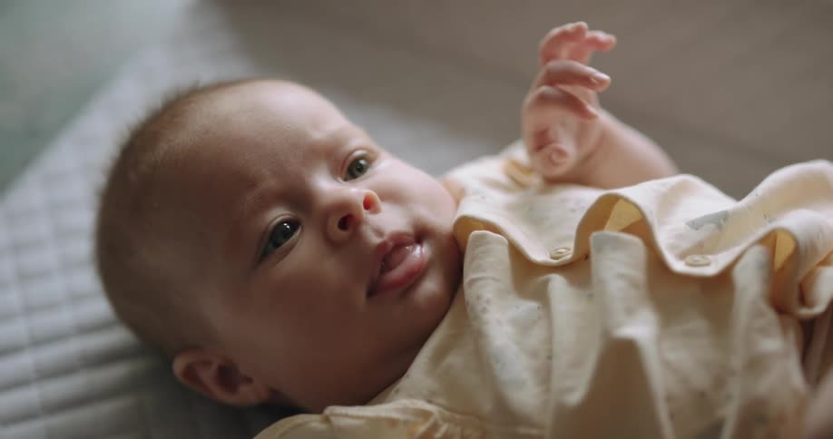 Light shines on the face of a baby lying on a bed and moving their hands