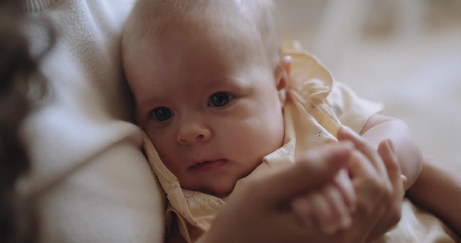 Mother with curly hair and white shirt holds baby in her arms