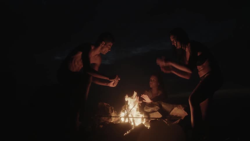 Three people warm themselves beside a campfire