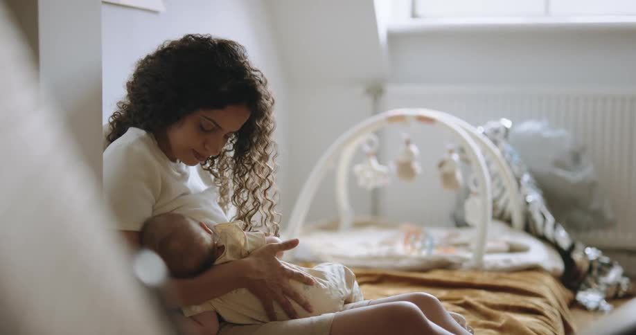 A woman cradles a baby while sitting on a bed indoors during the day