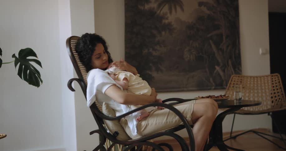 A woman cradles a baby in her arms while rocking back and forth in a rocking chair indoors during the day