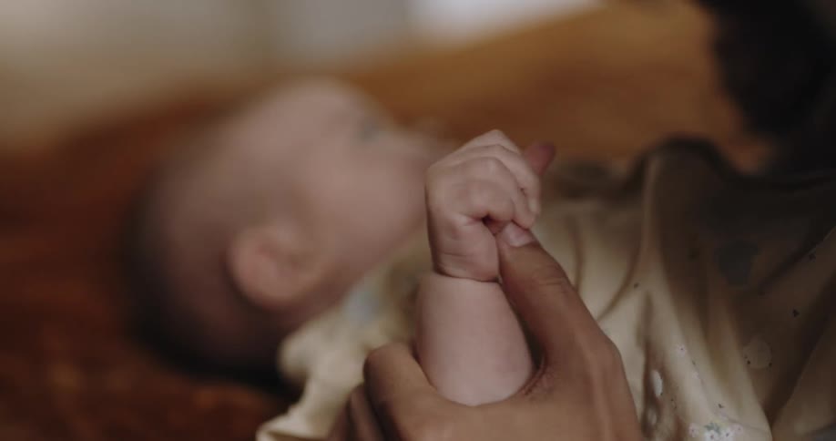 Mother leans over baby lying on its back to kiss child