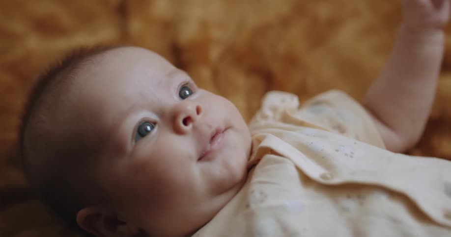 A baby is laying down making faces and smiling and moving their arms as they get excited