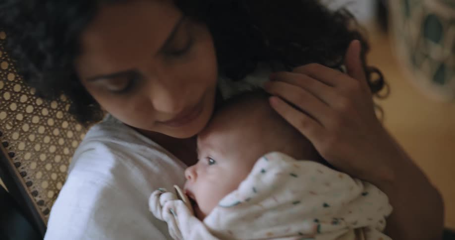 Mother rocks in rocking chair and holds baby sucking on a pacifier