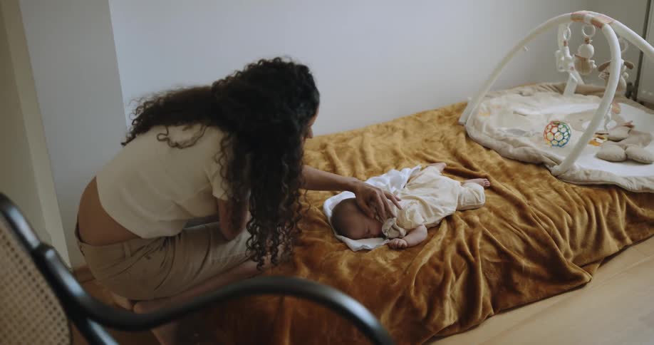 A woman brings her laptop over to check on her baby asleep on a bed